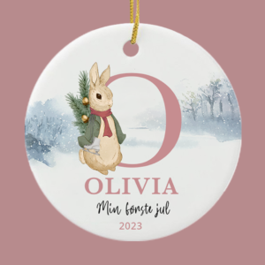 Keramikophæng med teksten "min første jul" og en fin lille kanin. På en lyserød baggrund.